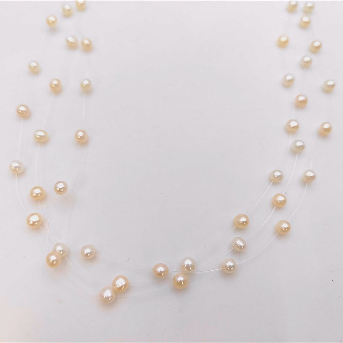 18 Karat Yellow Gold and Cultured Pearl Triple Strand Illusion Necklace: This triple-strand illusion necklace is constructed with cream-colored cultured pearls spaced along three clear monofilament strands. The pearls measure approximately 4.5mm to 5.5mm in diameter and fe
