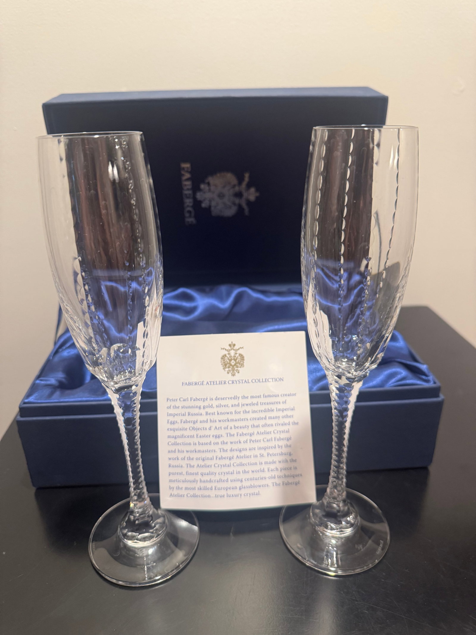 FABERGE ATELIER CRYSTAL CHAMPAGNE FLUTES, PAIR, BOXED: Pair of Faberge Atelier Crystal Collection champagne flutes in clear lead crystal. Slender tapered bowls with vertical optic ribbing and cut ovoid detail, raised on tall faceted and beaded stems over 