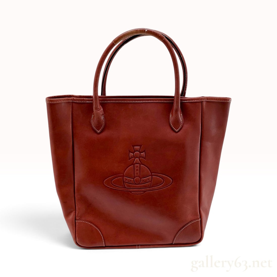 Vivienne Westwood Burgundy Leather Orb Tote Bag: This Vivienne Westwood tote bag is crafted from smooth burgundy leather featuring white contrast stitching throughout. The front panel is centered with a large, deeply embossed signature orb and cross