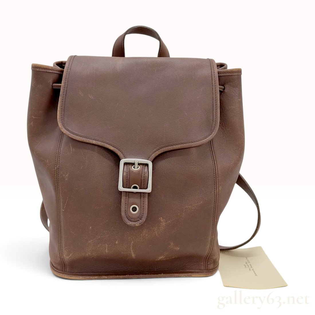 Vintage Coach Style 9064 Brown Glove Tanned Leather Flap Backpack with Hangtag: This vintage Coach Style 9064 backpack is constructed from brown glove-tanned cowhide leather. The design features a large front flap with a decorative buckle concealing a magnetic snap, a drawstring 