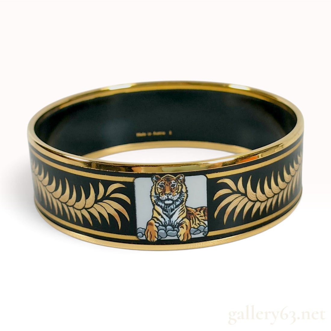 Vintage Hermes Tigre Royal Black Enamel Wide Bangle Bracelet with Box: This Hermes Tigre Royal wide bangle bracelet is crafted from black enamel with gold-tone metal borders. The exterior features two primary central motifs: a polychrome illustration of a resting tiger i