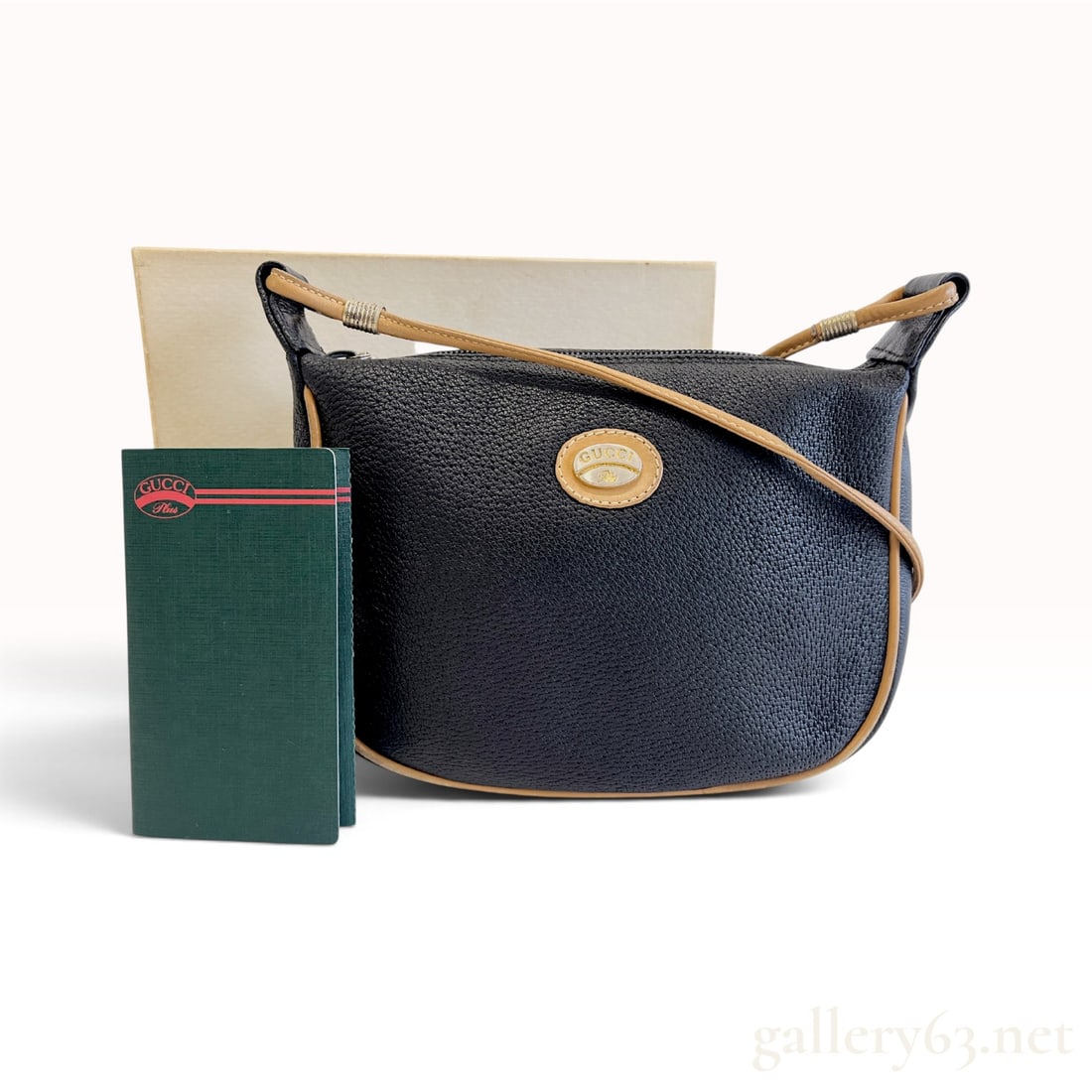Vintage Gucci Plus Black Pebbled Leather Crossbody Bag with Box and Booklet: This vintage Gucci Plus crossbody bag is crafted from black pebbled leather with tan smooth leather piping and a long shoulder strap. The bag features a curved silhouette with a top zipper closure ope