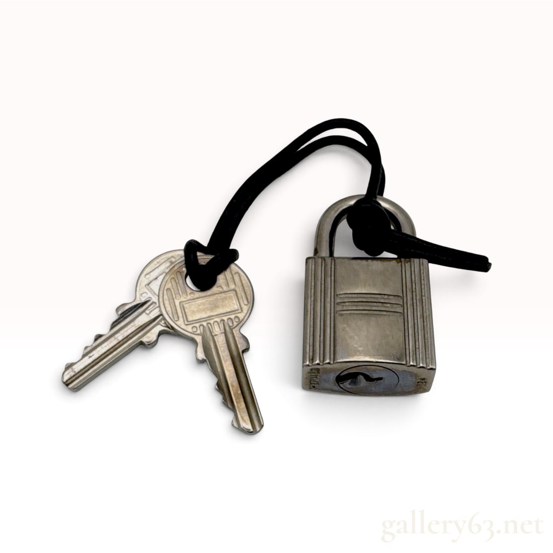 Hermes Silvertone Palladium Plated Padlock and Key Set 124: This Hermes padlock and key set is crafted from silvertone palladium-plated metal. The padlock features a rectangular body with vertical grooved texturing and a cylindrical keyhole at the base. It is 