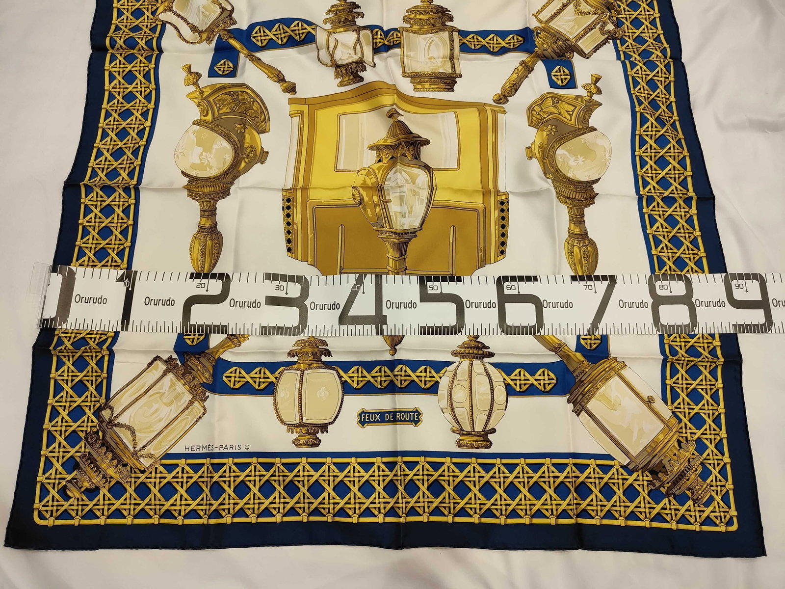 Vintage Hermes Feux de Route Navy and Gold Silk Carre 90: A Hermes silk carre 90 crafted from silk twill in the Feux de Route pattern. The design features a central white field decorated with detailed illustrations of ornate 19th-century carriage lamps and l