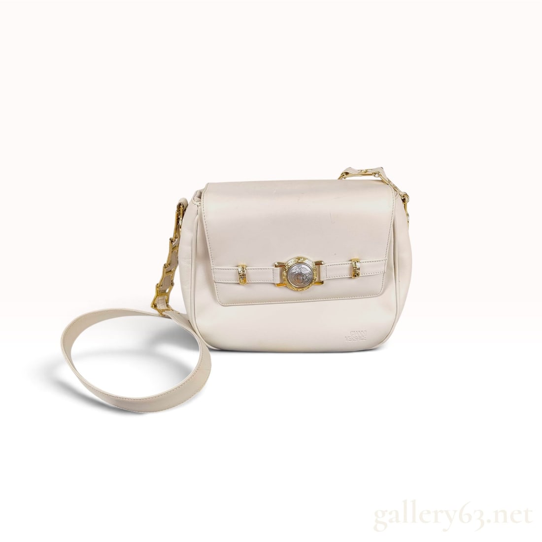 Vintage Gianni Versace Medusa Head Cream Leather Shoulder Bag: This Gianni Versace shoulder bag is constructed from cream leather and features a front flap closure with a decorative buckle strap element. The strap is adorned with a silver-colored Medusa head embl
