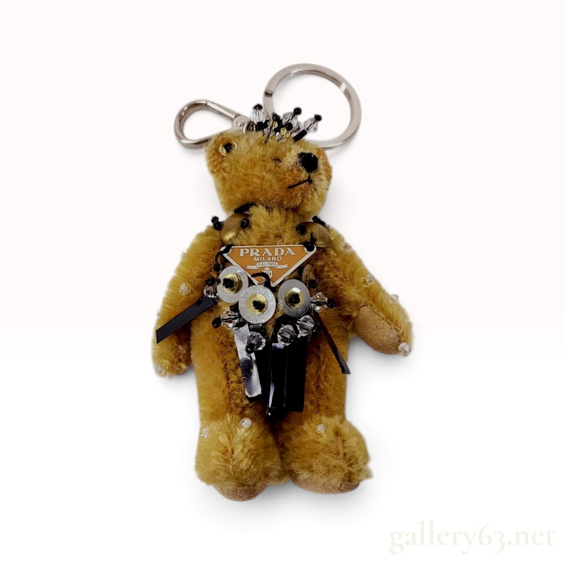 Prada Tan Mohair and Beaded Bear Bag Charm: This Prada bear bag charm is crafted from tan mohair plush with jointed limbs and felt paw pads. The bear is embellished with a necklace of sequins, faceted clear and black beads, and strips of black 