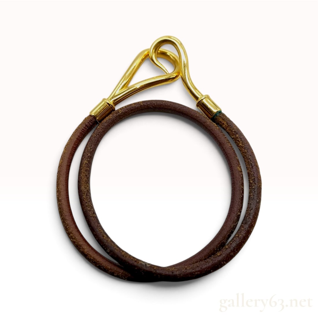 A Vintage Hermes Jumbo Brown Leather Double Wrap Bracelet: This Hermes double wrap bracelet is constructed from a continuous length of round brown leather cord designed to encircle the wrist twice. The piece features polished gold-tone hardware, including a J