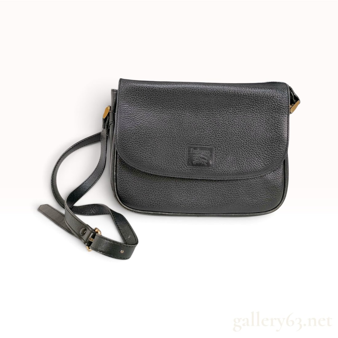 Vintage Burberrys Black Pebble Grain Leather Crossbody Bag: This Burberrys crossbody bag is crafted from black pebble grain leather with a structured rounded base and a flap front design. The bag features an adjustable leather shoulder strap secured with gold 
