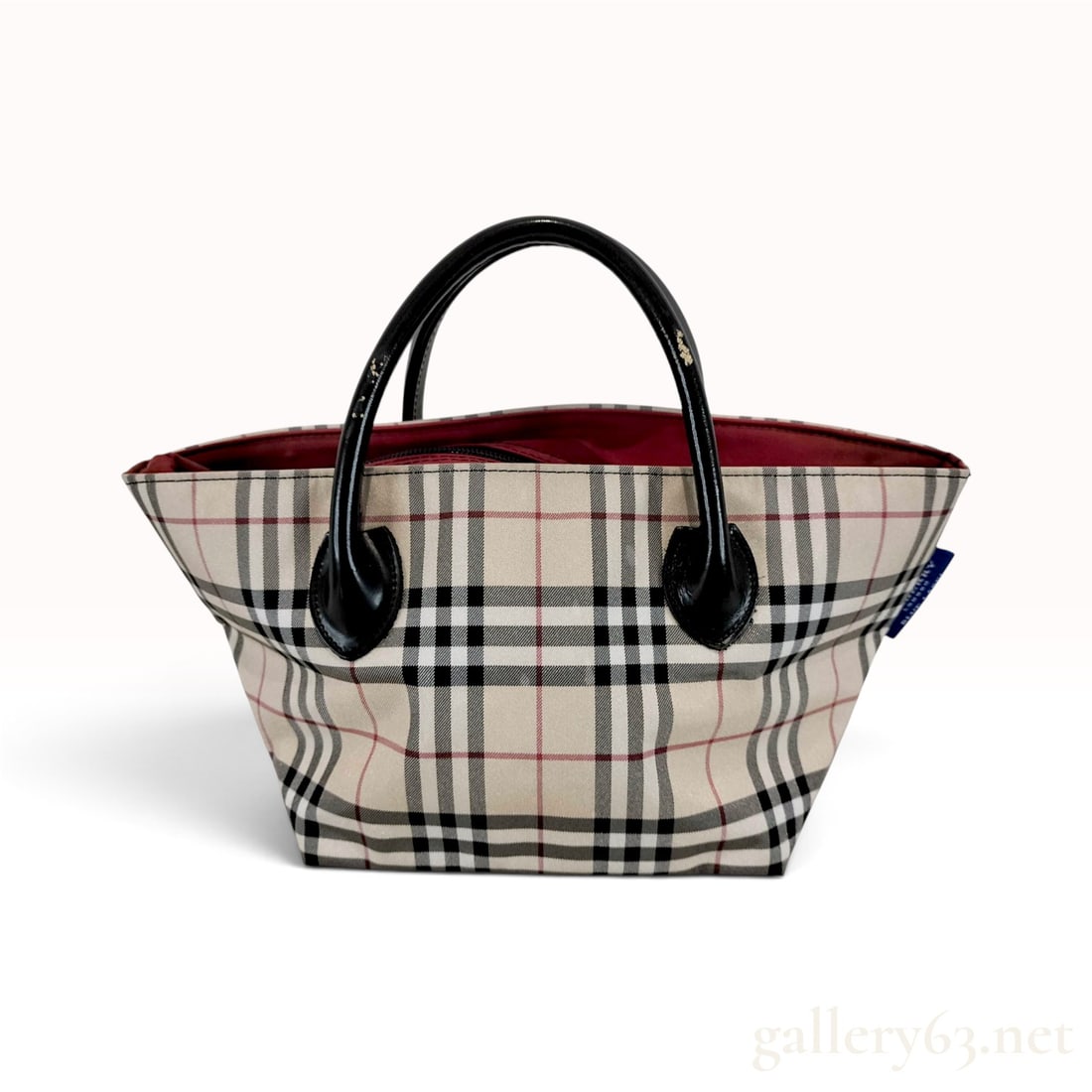 Burberry London Blue Label Nova Check Beige and Red Flared Tote Bag: This Burberry London Blue Label flared tote bag is crafted from check-patterned fabric with a solid red canvas base. The body features the signature beige, black, and red check pattern. It is designed