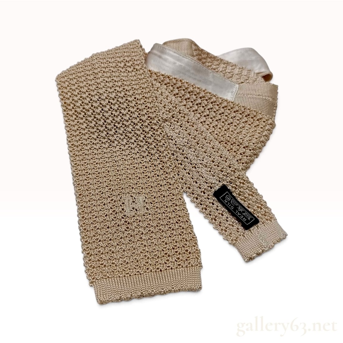 Hermes Embroidered H Logo Beige Silk Knit Necktie: This Hermes necktie is crafted from beige silk in a textured knit construction. The tie features a square-ended blade decorated with a tonal embroidered capital letter H. A cream silk satin ribbon is 