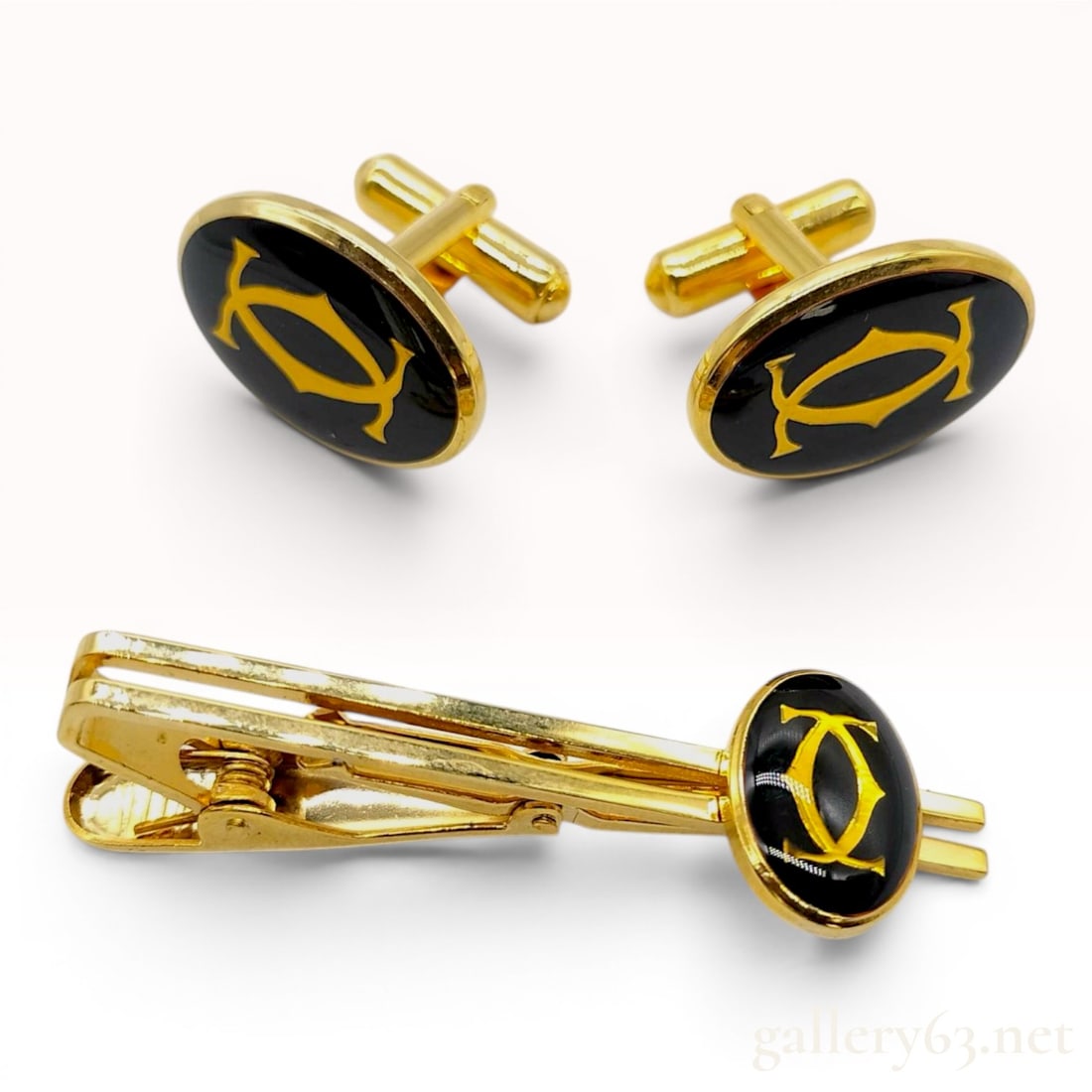 Cartier 2C Logo Gold-Tone and Black Lacquer Cufflink and Tie Clip Set: A trio of Cartier men's accessories including a matching pair of cufflinks and a tie clip. Each item is centered with an oval plaque featuring a black lacquer or enamel finish, decorated with a gold-t