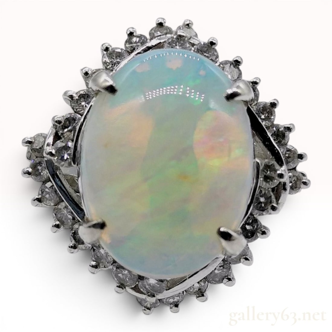 A 2.41ct Australian Opal and.50ctw Diamond Halo Cocktail Ring in Platinum: A platinum cocktail ring centering an oval cabochon Australian opal weighing 2.41 carats. The central stone displays a milky base with play-of-color showing flashes of green, orange, and yellow. The o