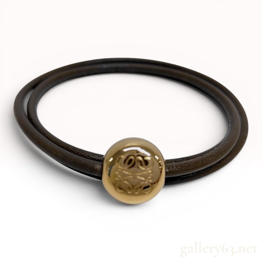 Loewe Anagram Pebble Leather Bracelet: A designer double-wrap bracelet by the Spanish luxury fashion house Loewe. The piece is constructed from a dark brown round leather cord and features a single spherical gold-tone metal bead, a signatu