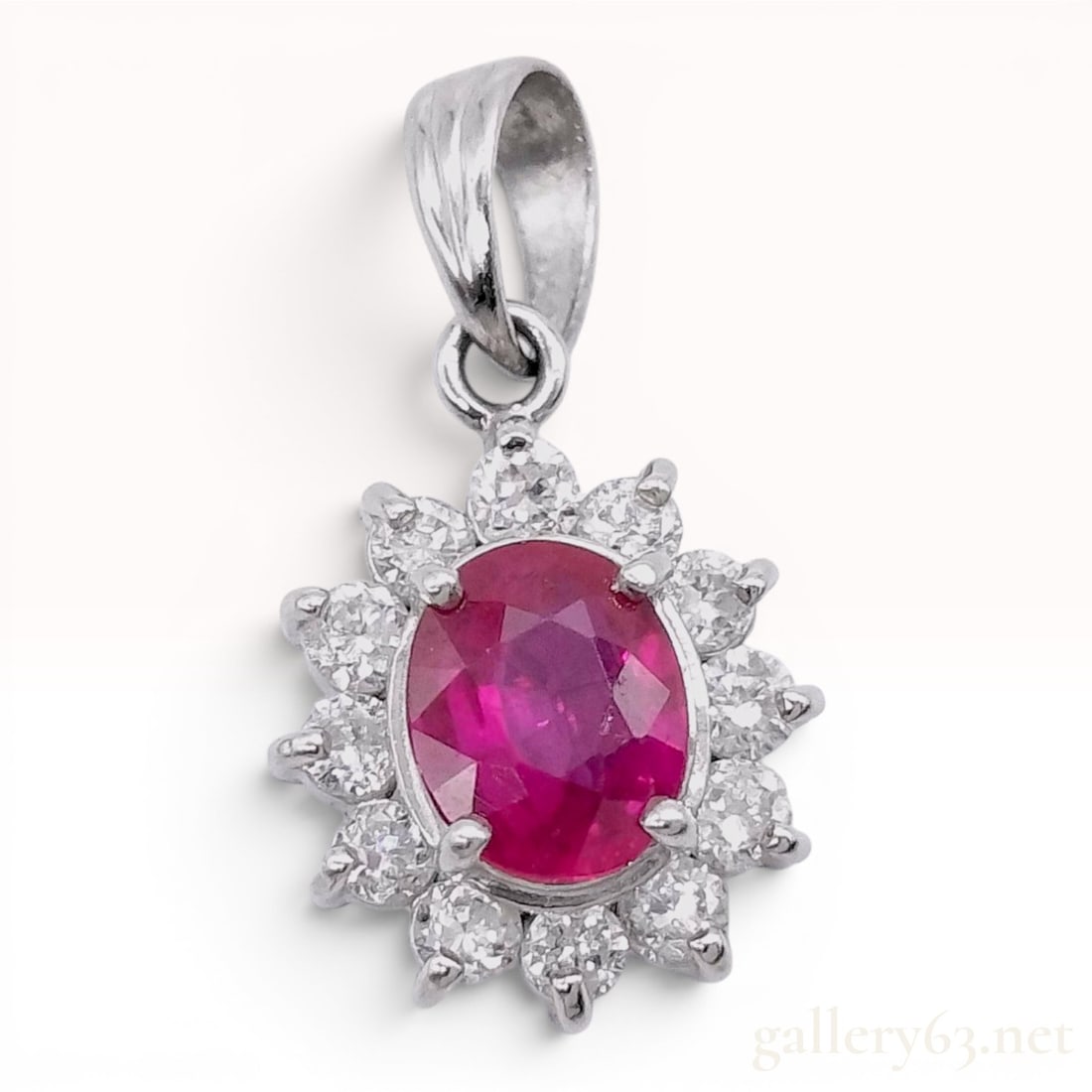 Platinum Ruby and Diamond Halo Cluster Pendant: A platinum cluster pendant featuring a central oval-cut ruby measuring approximately 5mm by 4mm. The ruby is secured in a four-prong setting. The center stone is encircled by a starburst-style halo of