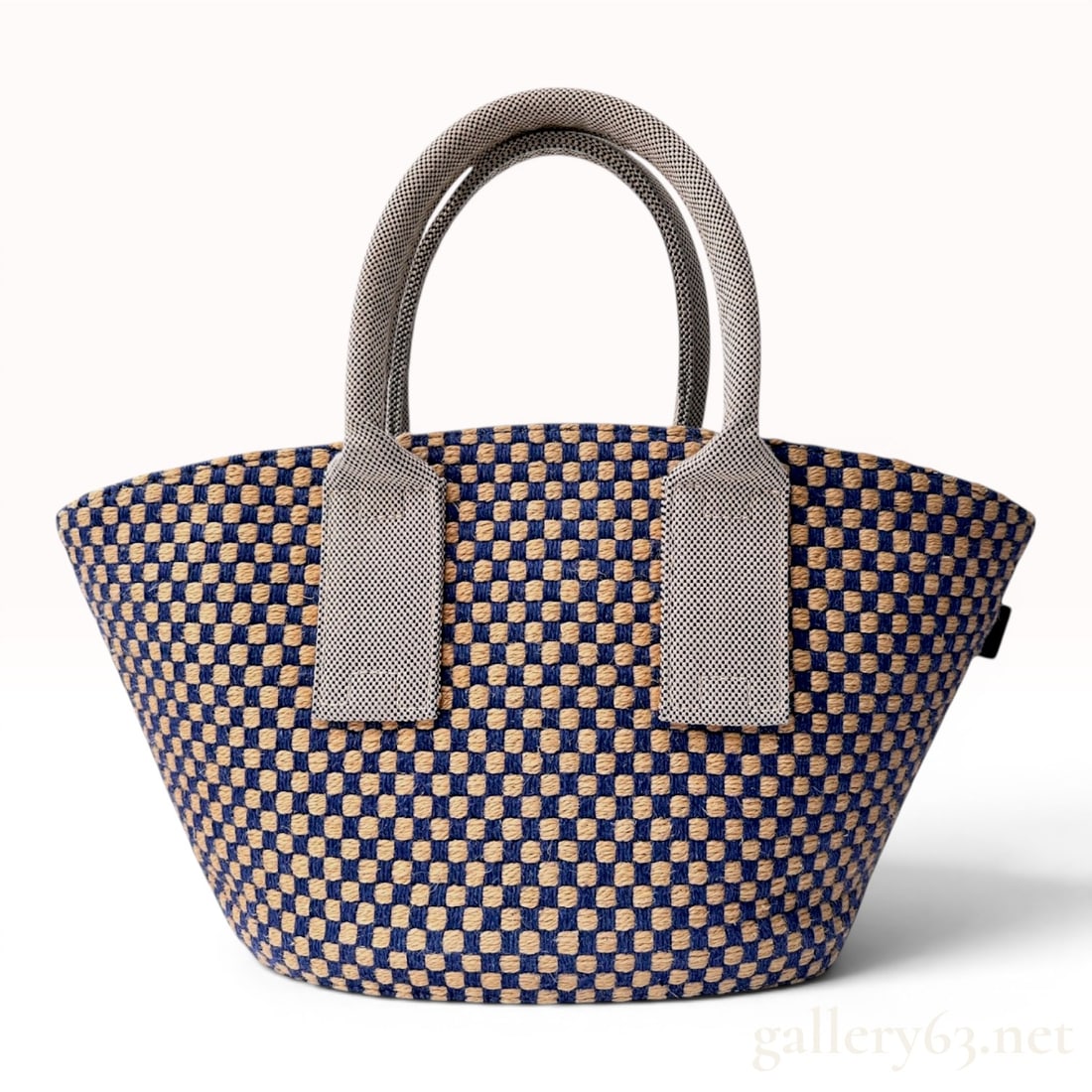 Hermes Basket Weave Jute Checkerboard PM Tote Bag: A Hermes basket weave tote bag crafted from woven jute cord in a navy blue and natural tan checkerboard pattern. The bag features a flared silhouette with an oval-shaped reinforced base and wide integ