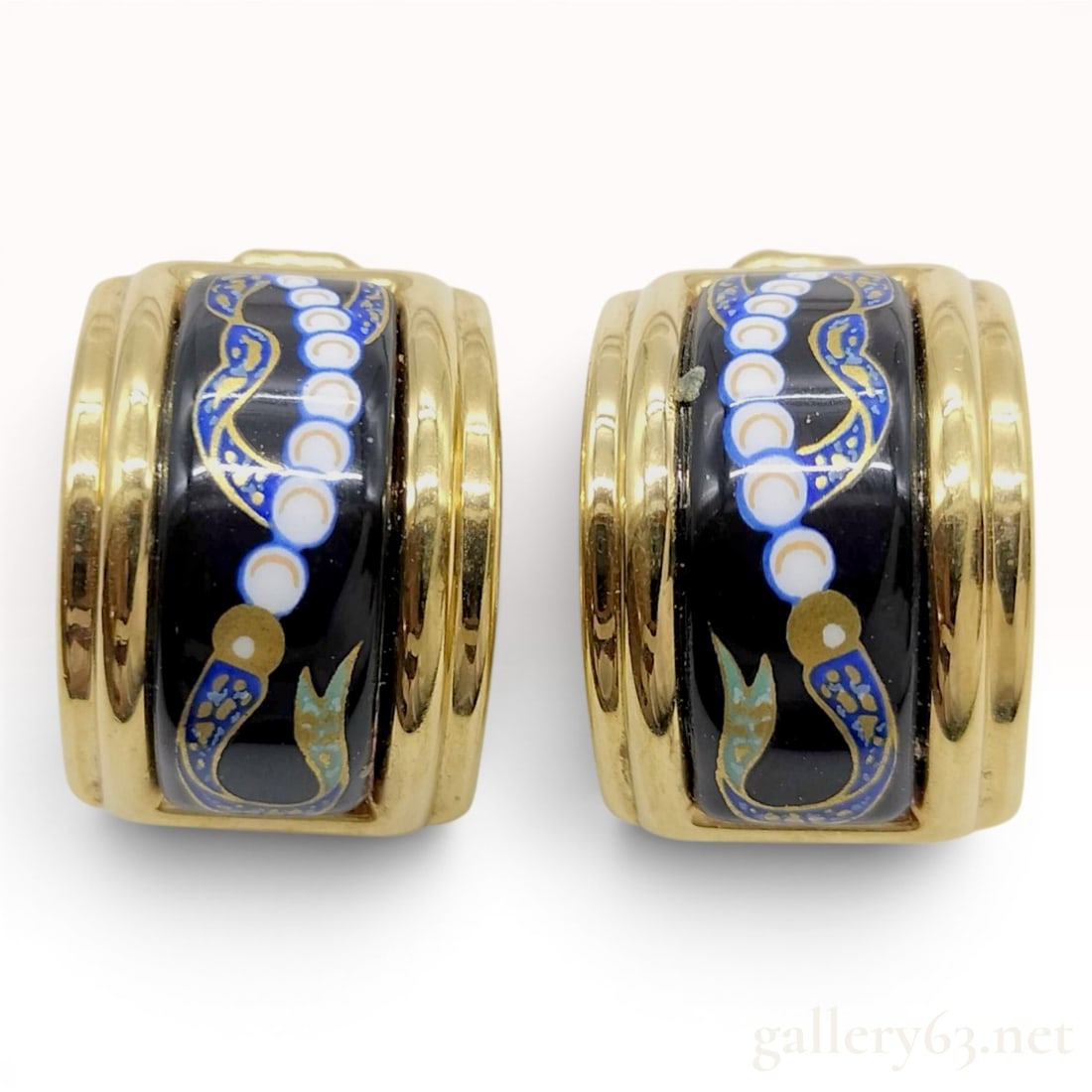 A Pair of Hermes Gold-Plated Enamel Clip-On Hoop Earrings: A pair of Hermes gold-plated enamel clip-on hoop earrings. Each earring features a curved metal frame housing a decorative enamel inlay. The pattern displays a series of white circular motifs against 