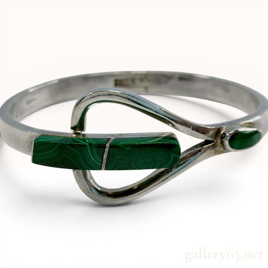 Taxco Modernist Sterling Silver and Malachite Hinged Bangle Bracelet: This modernist hinged bangle bracelet is crafted from sterling silver and features decorative malachite elements. The piece is designed in a bypass style, with one side of the band forming an elongate