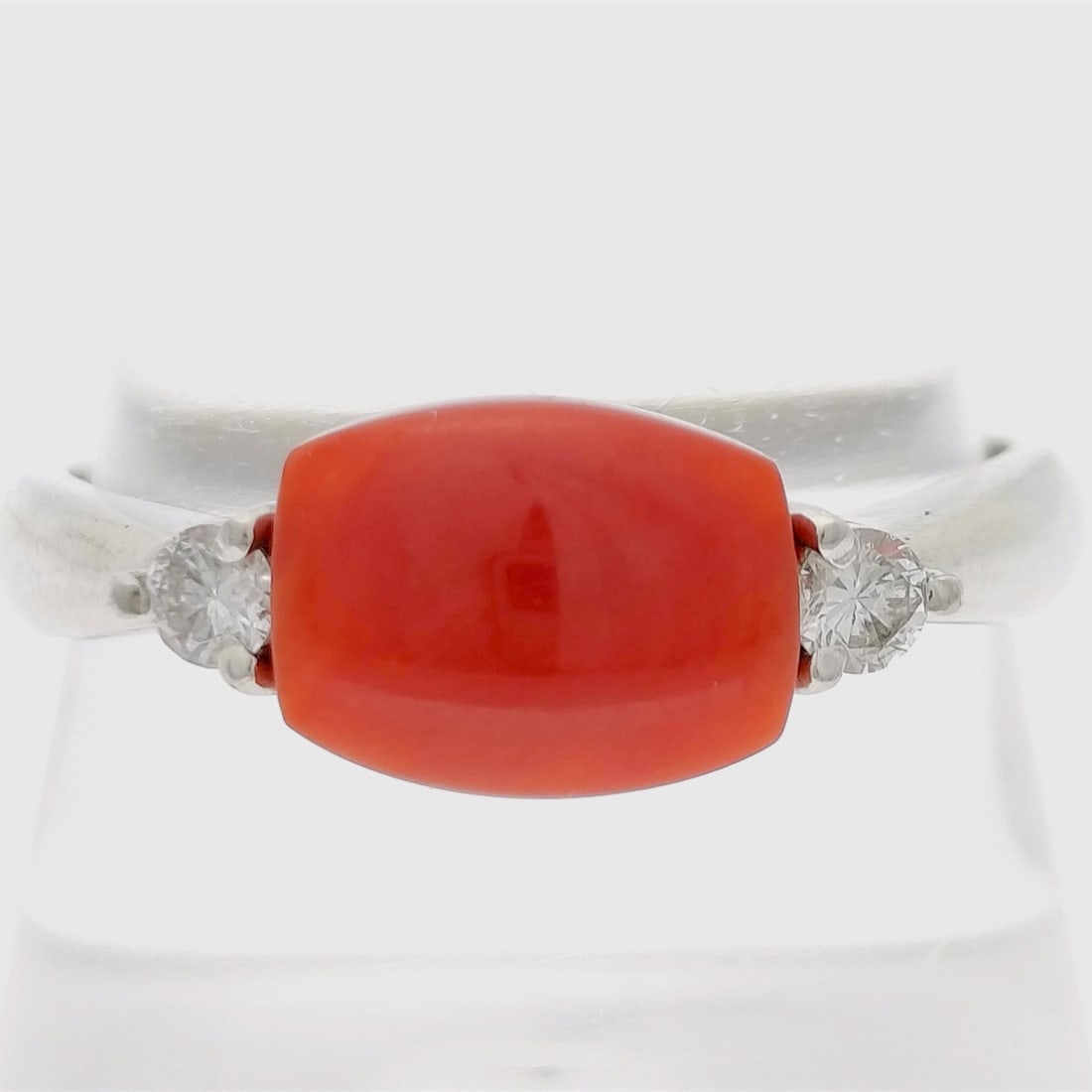 Antique Red Coral Cabochon and Diamond Platinum Ring: This platinum ring features a central barrel-shaped antique red coral cabochon. The central stone is set within a bridge-style mounting that includes a decorative open-work under-gallery. The coral is