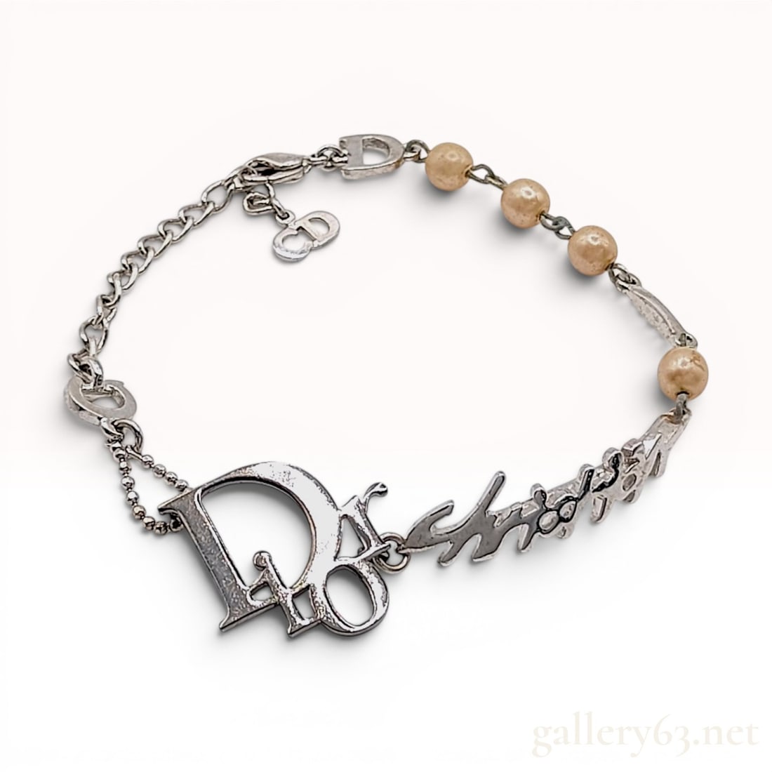 Christian Dior Silver-Tone Logo and Faux Pearl Charm Bracelet: A designer costume jewelry bracelet by Christian Dior crafted in silver-tone base metal. The link chain design features a large, stylized script Dior logo as a central focal point. The bracelet includ