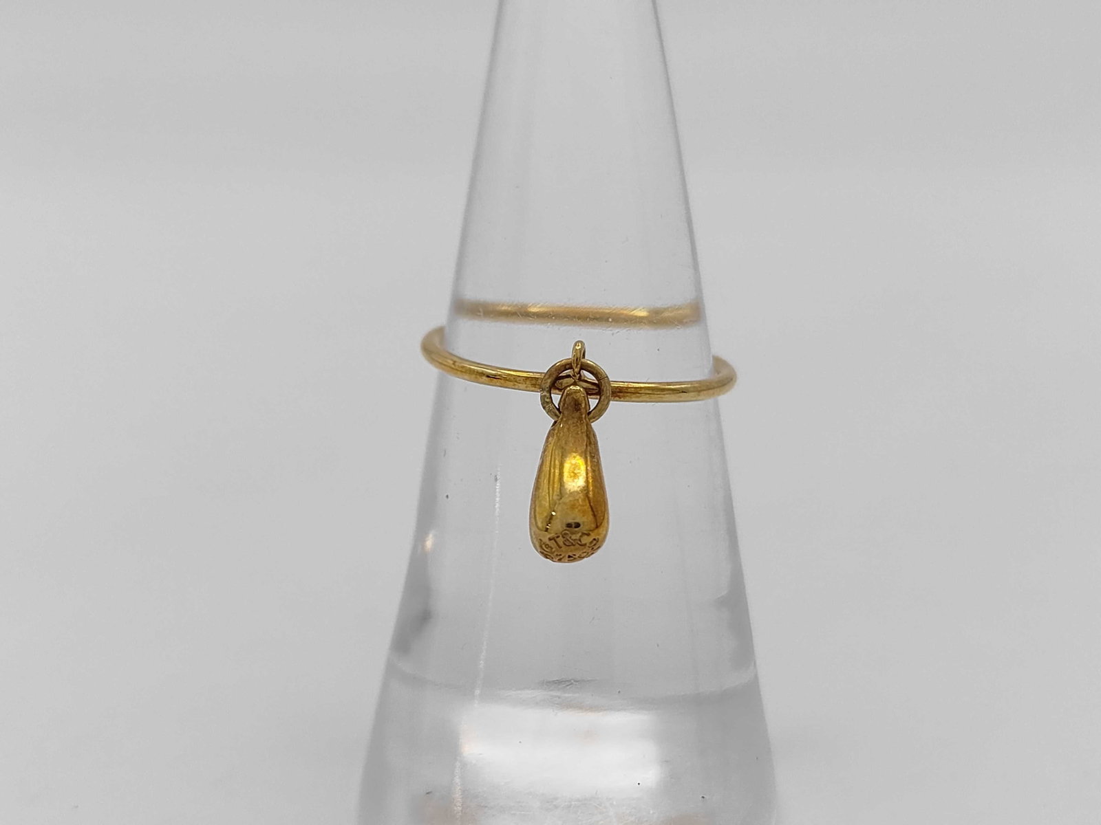 Tiffany and Co. 18K Yellow Gold Teardrop Ring with Box: Tiffany and Co. 18 karat yellow gold dangle charm ring from the Elsa Peretti Teardrop collection. The piece features a thin wire-style band with an integrated loop at the center that holds a solid tea