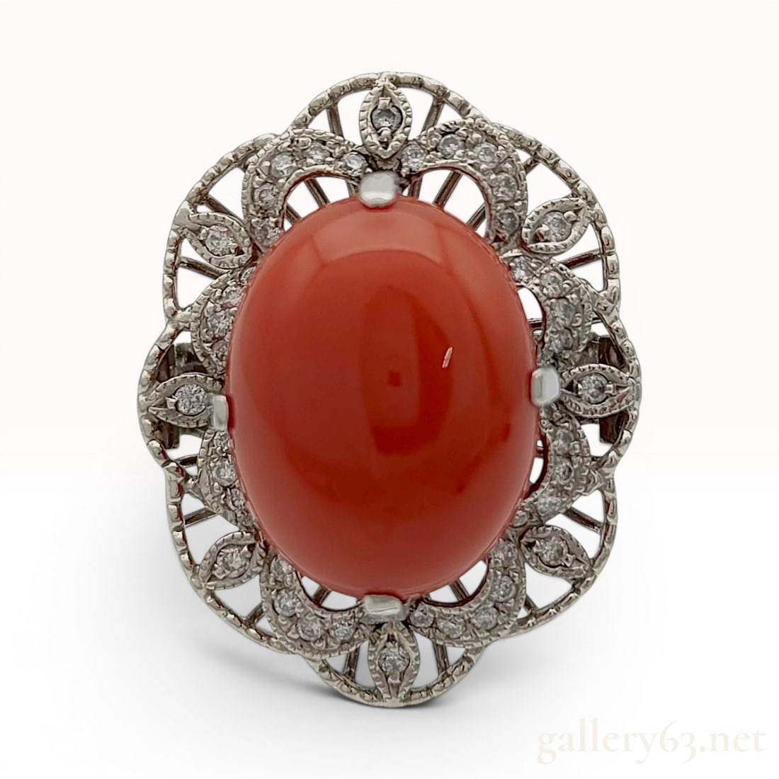 Antique Red Coral and Diamond Cocktail Ring in Pt900 Platinum: An antique cocktail ring centering a large oval cabochon-cut red coral weighing 14.77 carats. The vibrant red stone is set within a Pt900 platinum mounting featuring an ornate, pierced openwork frame.