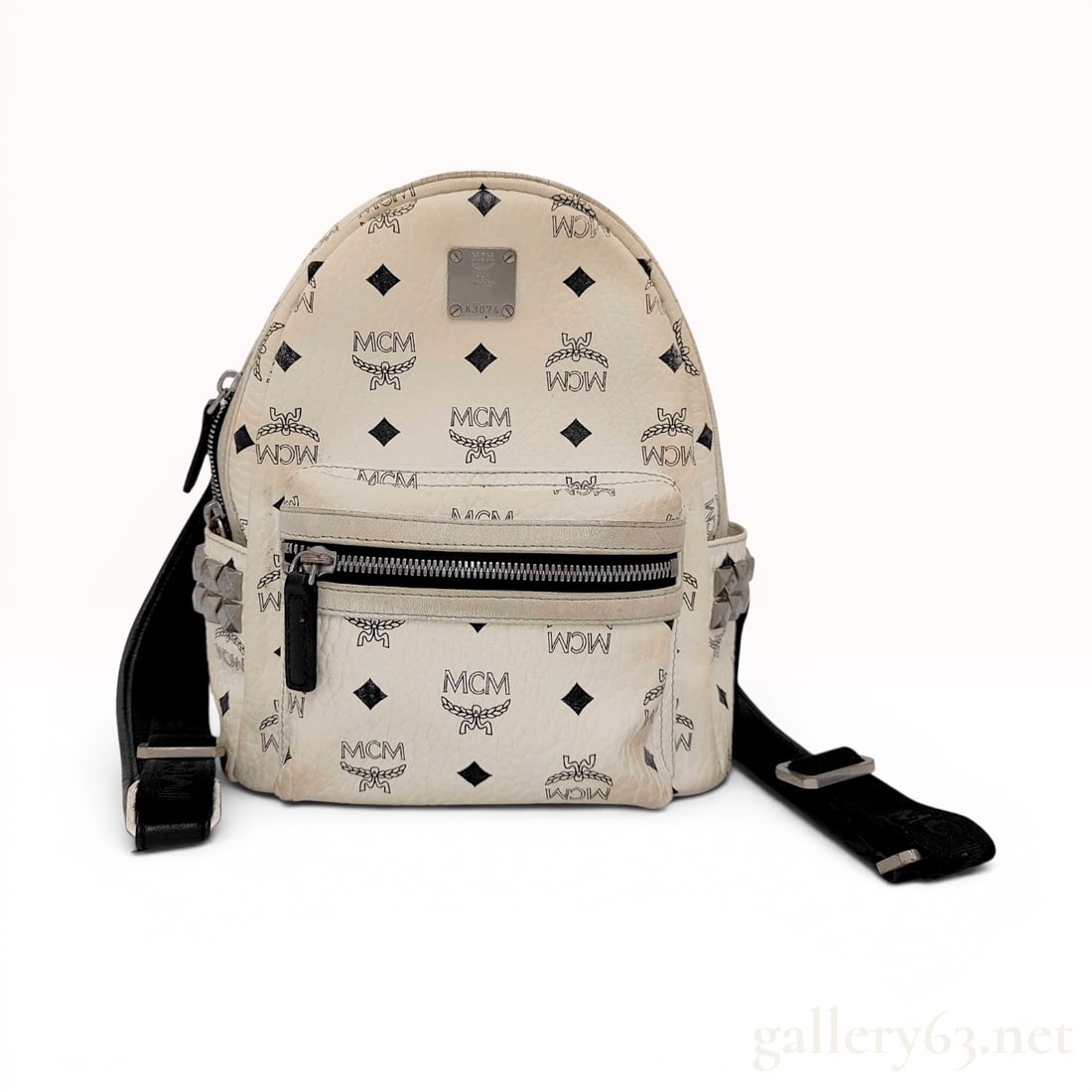 MCM White Visetos Coated Canvas Small Stark Studded Backpack: This small-sized Stark backpack is constructed from white Visetos monogram coated canvas with contrasting black leather accents. The exterior features a front zippered pocket and two side slip pockets