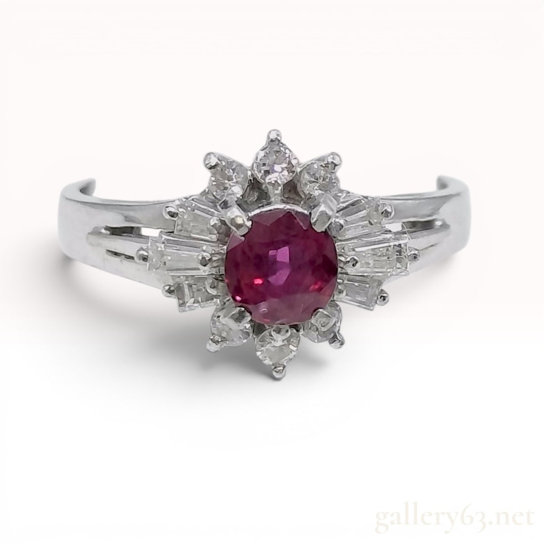 Platinum Ruby and Diamond Ballerina Style Cocktail Ring: A platinum cocktail ring featuring a central round-cut ruby. The ruby is secured in a four-prong setting and encircled by a tiered ballerina style halo. This halo is composed of a mix of round brillia