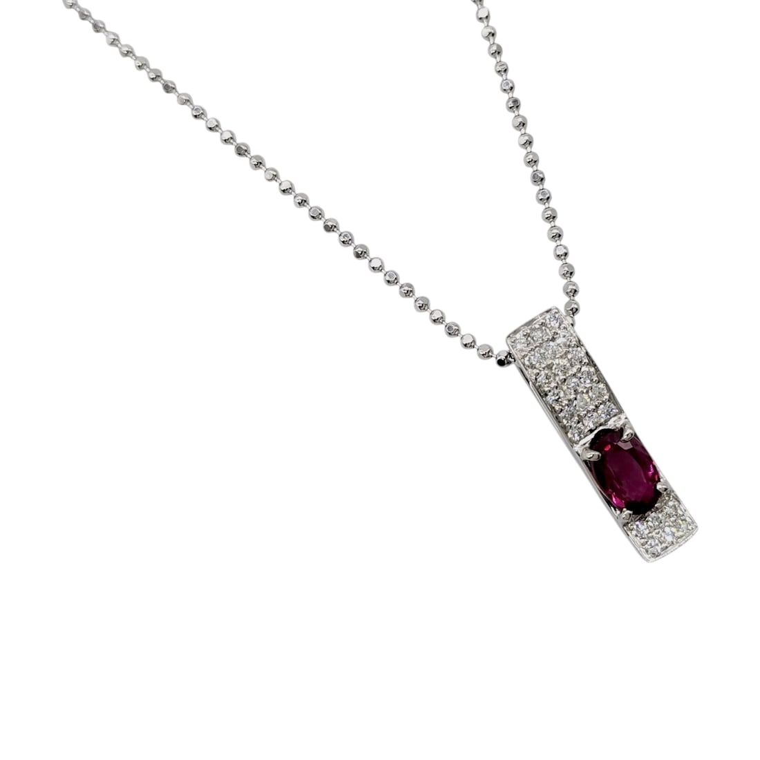 Platinum Ruby and Diamond Bar Pendant Necklace: This contemporary necklace features a rectangular bar pendant crafted in platinum with a slightly curved profile. The center of the piece is set with a single oval-cut ruby, weighing approximately 0.7