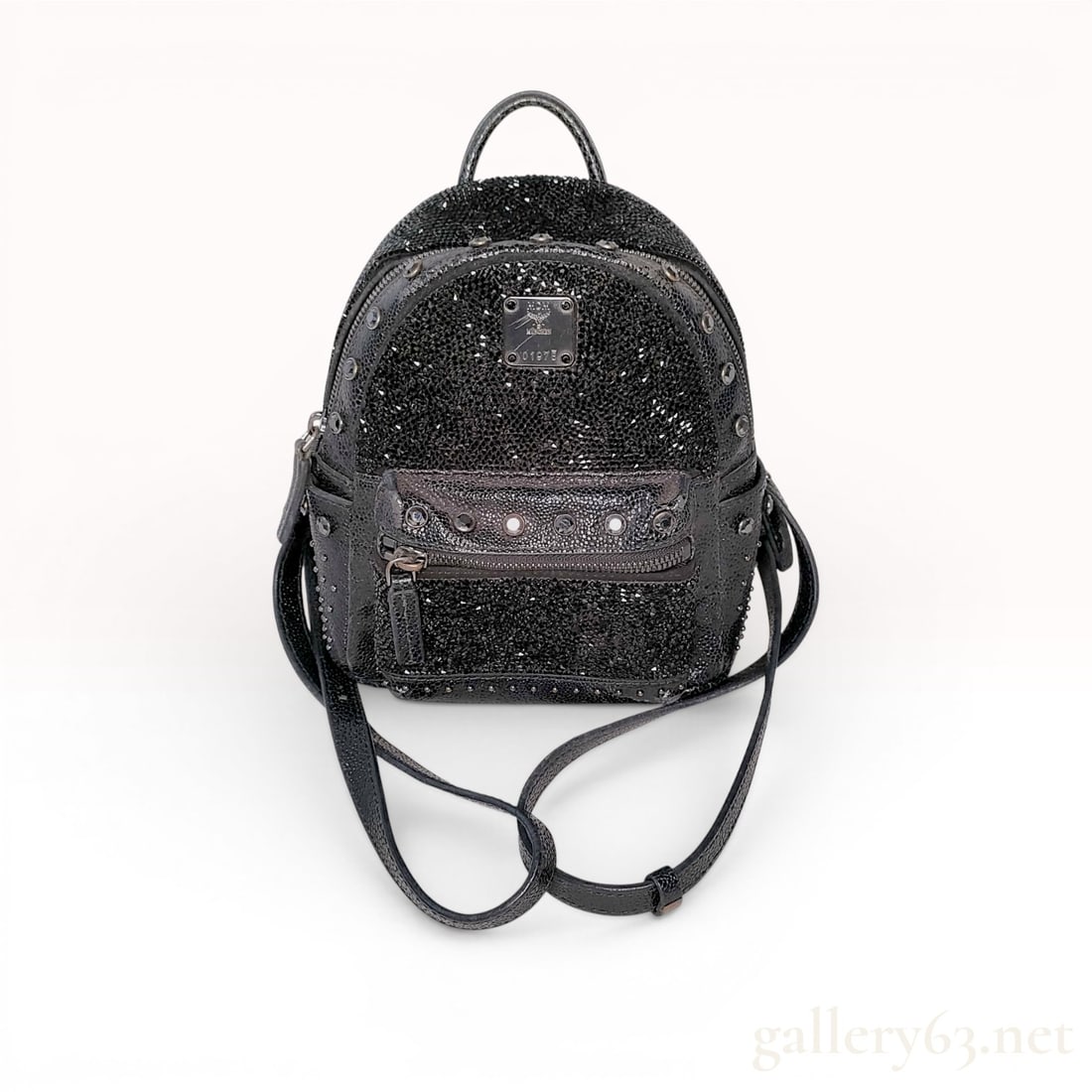 MCM Stark Bebe Boo X-Mini Crystal Embellished Black Leather Backpack: An MCM Stark Bebe Boo X-Mini backpack constructed from black leather with a pebbled shagreen texture. The upper front portion is densely embellished with multifaceted black crystals. The bag features 