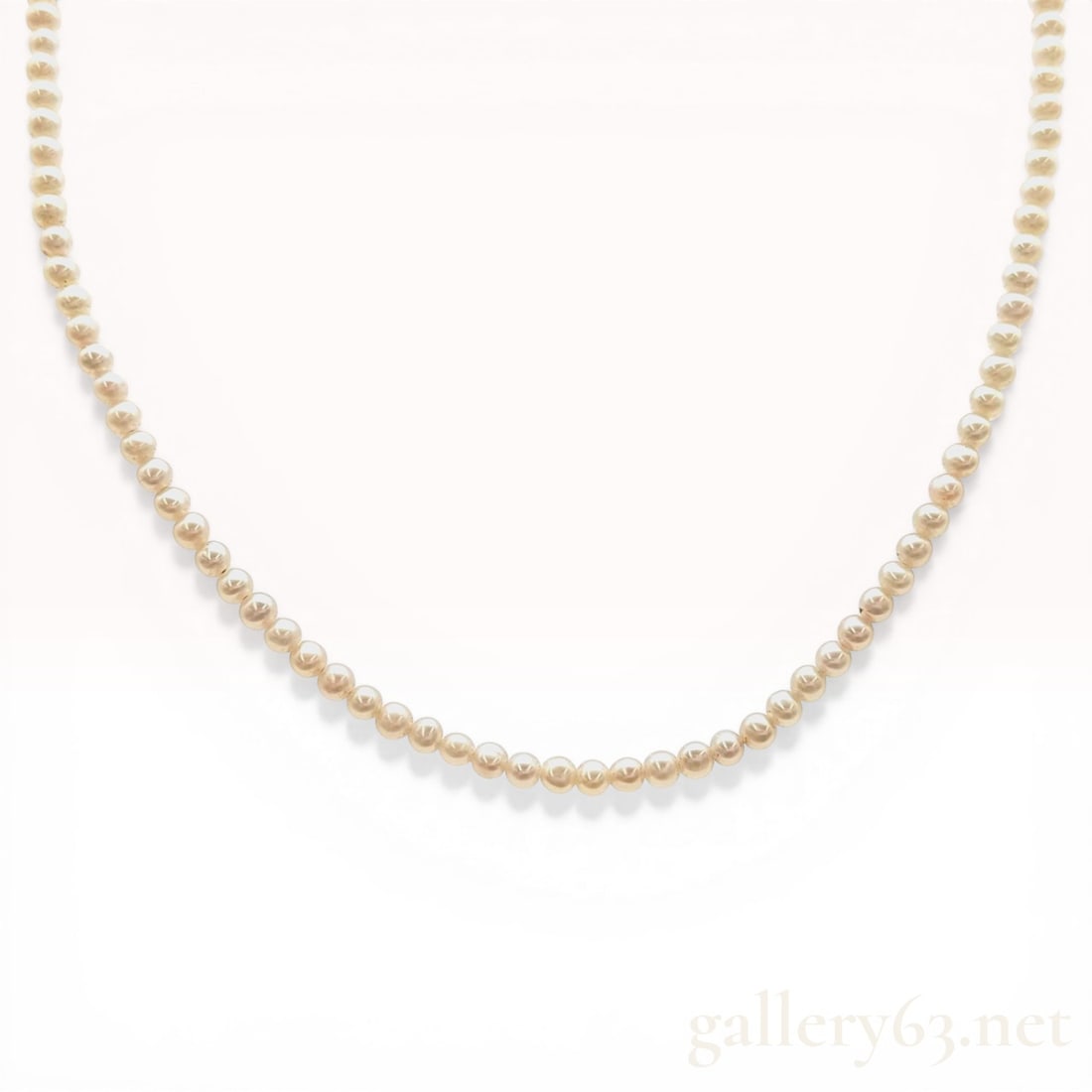 Cultured Pearl Single Strand Necklace with 18 Karat Yellow Gold Clasp: Cultured pearl single-strand necklace featuring uniform round to near-round pearls with a creamy white body color. The necklace is strung on a white cord and finished with an 18 karat yellow gold