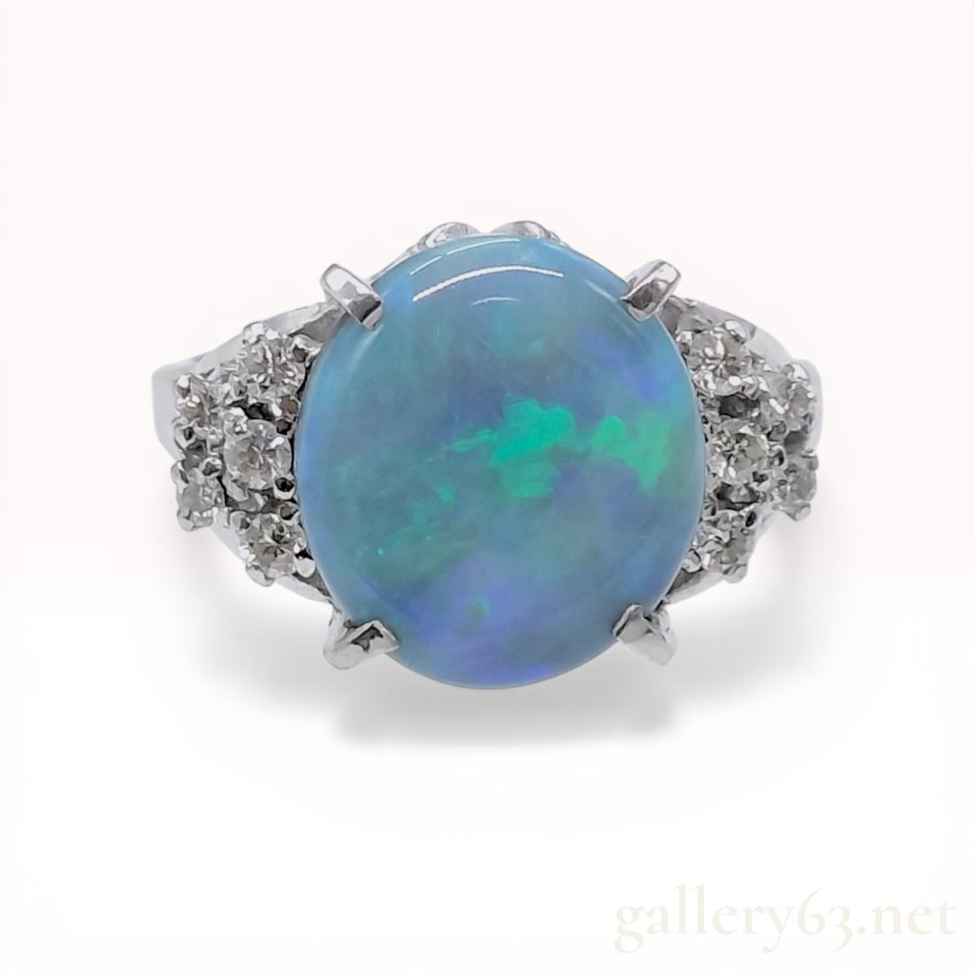 Opal and Diamond Platinum Cocktail Ring: Vintage-style cocktail ring featuring a central oval cabochon-cut opal and diamond accents set in platinum. The opal exhibits a green and blue play-of-color and is secured by four double-prongs,