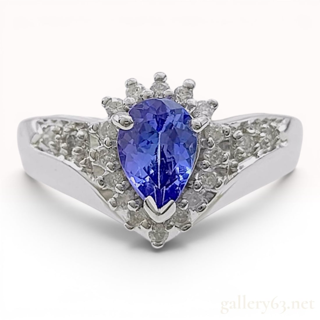 Tanzanite and Diamond 14 Karat White Gold Ring: This 14 karat white gold ring features a central pear-shaped tanzanite of violet-blue hue, secured in a three-prong setting. The gemstone is encircled by a tiered halo of round brilliant-cut diamond