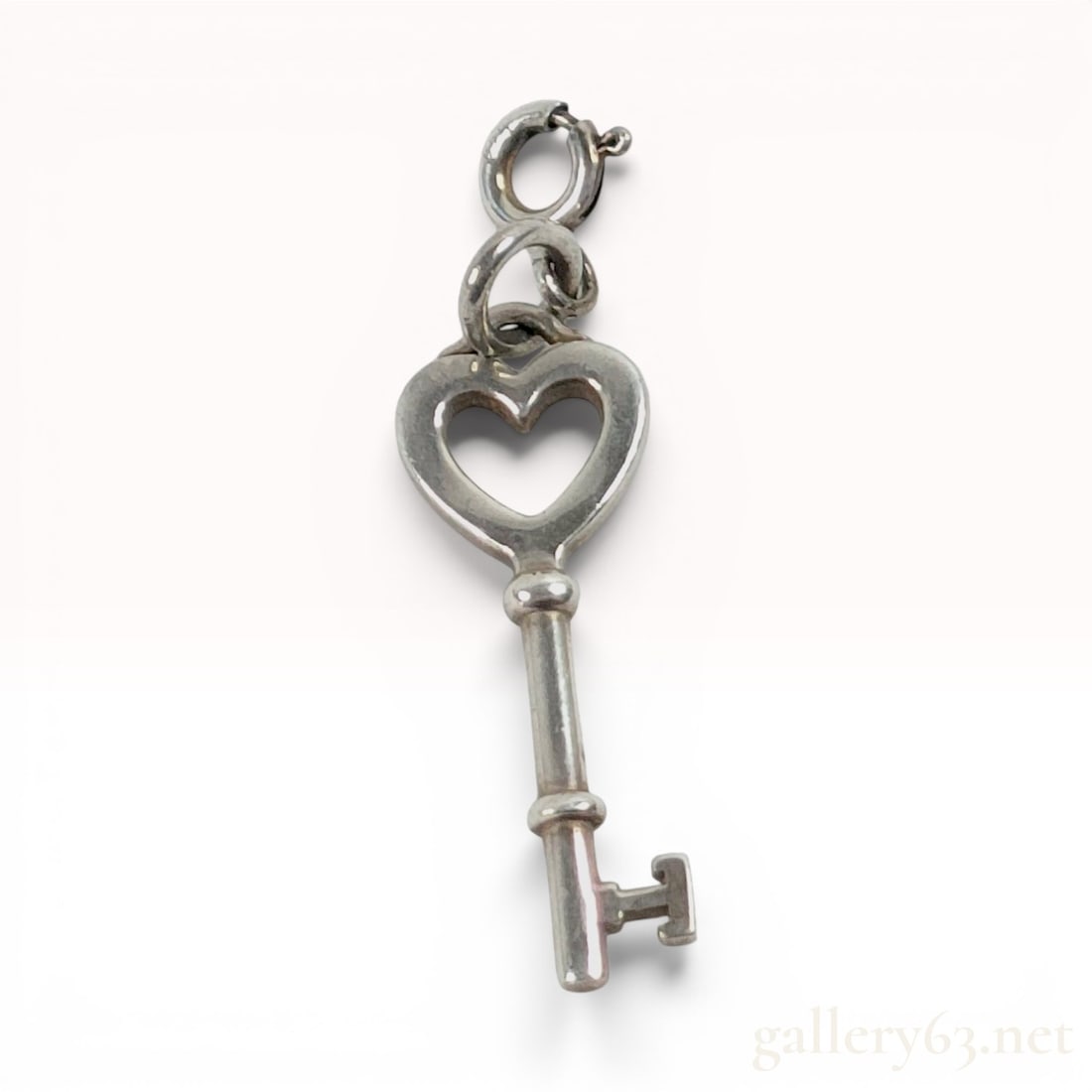 Tiffany and Co. Sterling Silver Tiffany Keys Mini Heart Key Charm Pendant: This sterling silver charm is part of the Tiffany and Co. Tiffany Keys collection. The design features a polished open heart-shaped bow surmounting a cylindrical shaft. The shaft is detailed with two 