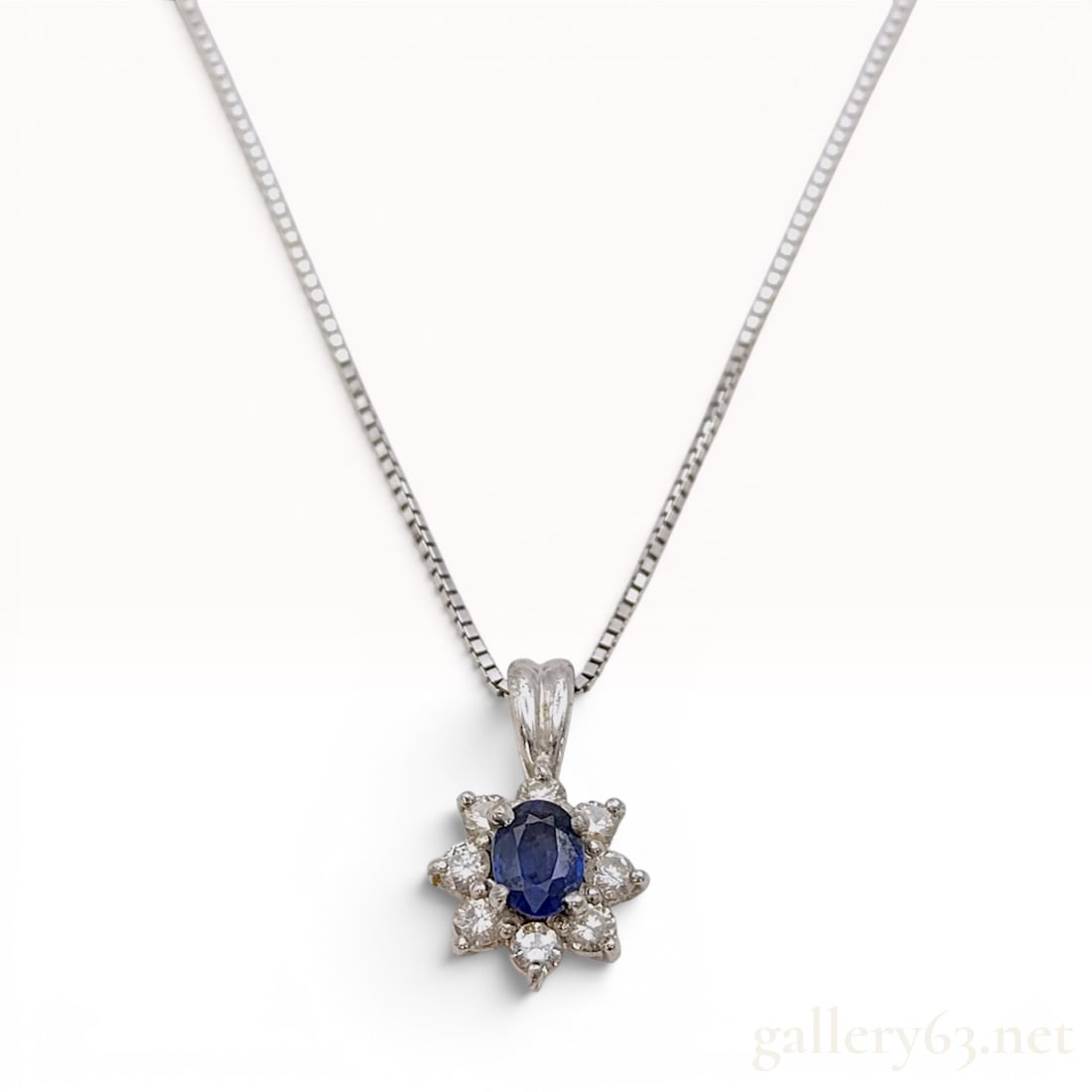 Sapphire and Diamond Halo Pendant in Platinum on an 18K White Gold Box Chain: This pendant necklace features a central oval-cut blue sapphire, weighing approximately 0.30 carats. The sapphire is held in a four-prong setting and is surrounded by a halo of eight round brilliant-c