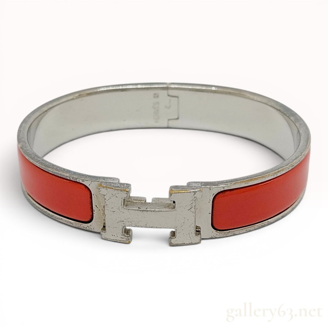 Hermes Red Enamel and Palladium-Plated Clic H Bangle Bracelet: A Hermes Clic H hinged bangle bracelet featuring two sections of vibrant red enamel inlay set within a silver-tone palladium-plated metal frame. The front of the bracelet is accented with the signatur