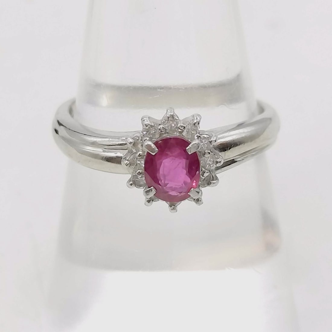 Platinum.60ct Ruby and.15ctw Diamond Cluster Ring: This cluster ring is crafted in Pt850 platinum. The setting features a central oval-cut pinkish-red ruby held in a four-prong mount with split prongs at the corners. The center stone is bordered by a 
