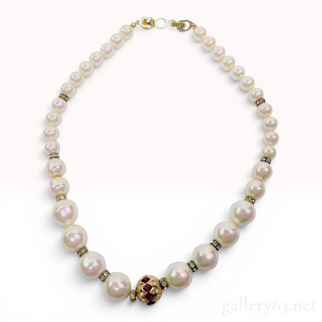 Christian Dior Graduated Faux Pearl Necklace with Rhinestone and Red Stone Accents: A Christian Dior costume necklace featuring a strand of graduated white faux pearls with high luster and pink and green overtones. The necklace centers on a gold-tone globular bead set with square-cut