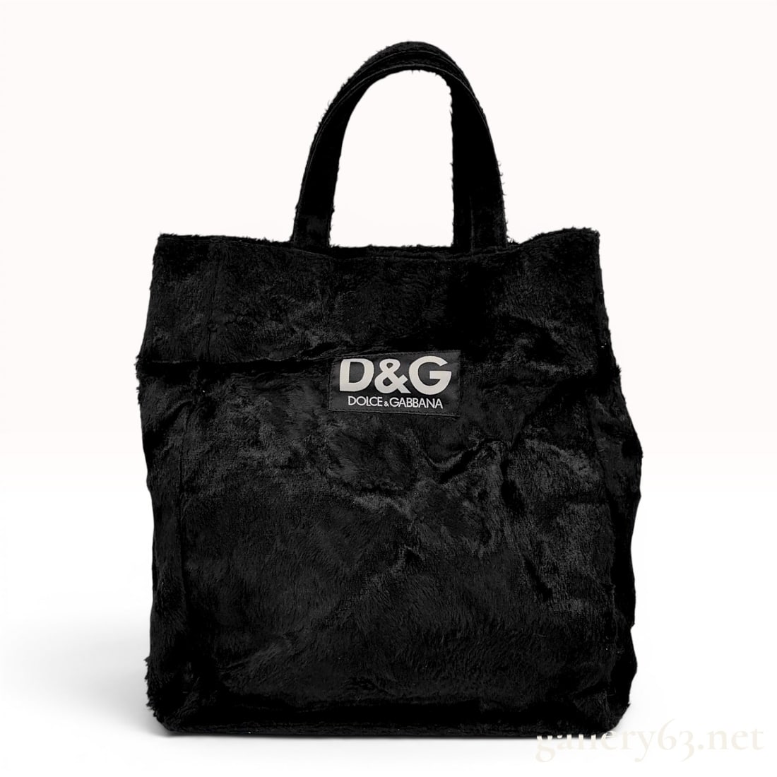 D&G Dolce and Gabbana Black Faux Fur Tote Bag: This black faux fur tote bag features a plush exterior and twin top handles. The front of the bag displays a black fabric patch with the white logo reading D&G DOLCE & GABBANA. The bag includes a blac
