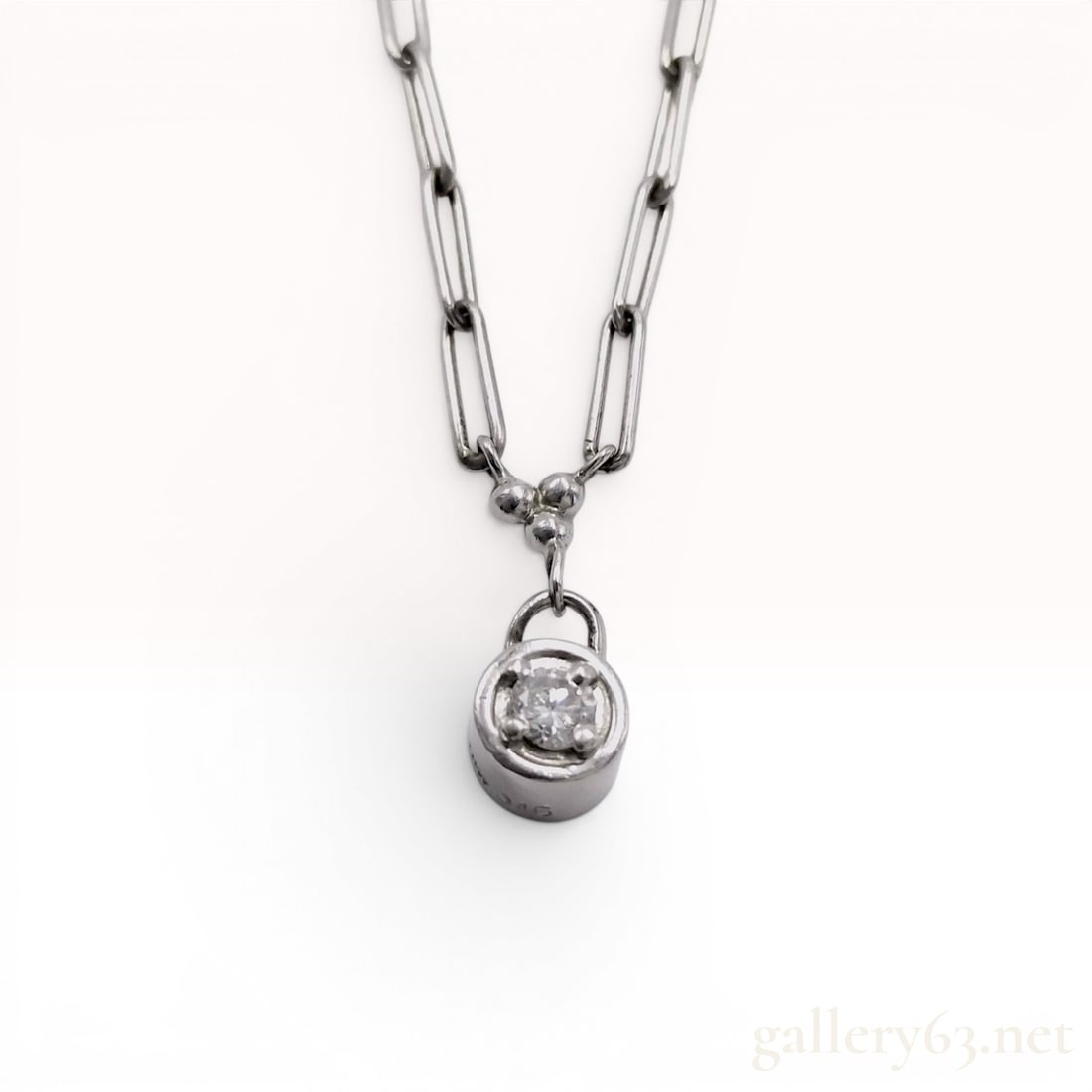 Platinum and Diamond Solitaire Pendant Necklace with Paperclip Link Chain: This contemporary pendant necklace is crafted from platinum and features a single round brilliant-cut diamond. The diamond is bezel-set within a cylindrical mounting that incorporates four small inter