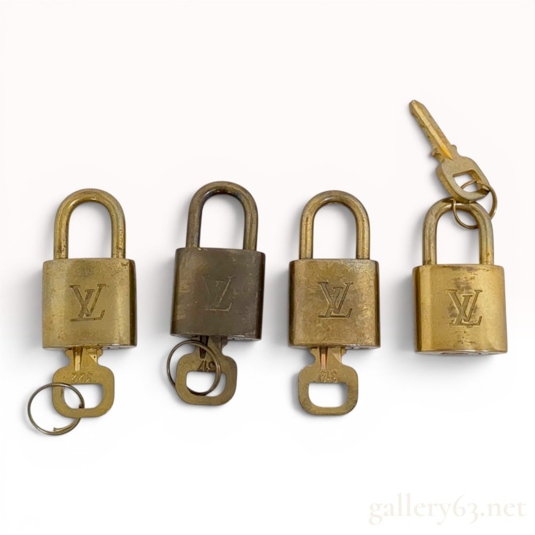 A Set of Four Louis Vuitton Brass Padlocks with Matching Keys: A set of four vintage brass padlocks with matching keys by Louis Vuitton. Each padlock features a rectangular body with a rounded top shackle. The front of each lock is decorated with the embossed int