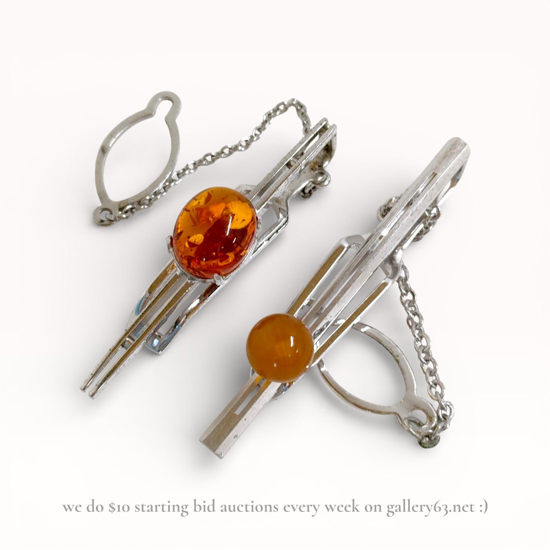 Pair of Sterling Silver Tie Pins with Cabochon Amber Stones: Tie pin pair featuring elongated sterling silver bar forms fitted withwarm amber round cabochon stones. Each pin having a chain and loop backing for secure attachment. Polished metal surfaces with sim