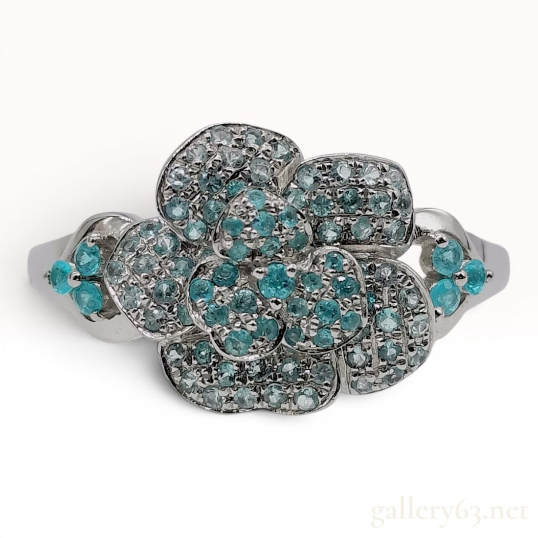 A Platinum and Paraiba Tourmaline Flower Cluster Ring: A platinum cocktail ring designed as a stylized multi-petaled flower head. The petals and center are pave-set with numerous small, round-cut neon blue Paraiba tourmalines and diamonds. The ring constr