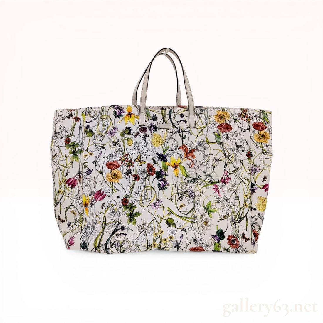 Gucci Flora Canvas Large Tote Bag: Large Gucci shopper tote crafted from off-white canvas featuring the multi-colored Flora botanical print. The bag is designed with dual off-white leather top handles, dark edge glazing, and a natural