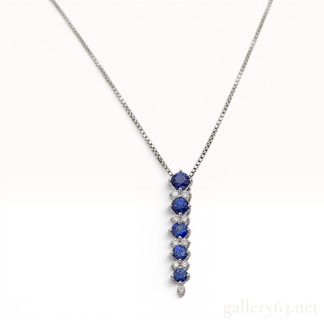 Platinum Blue Sapphire and Diamond Linear Drop Pendant Necklace: This platinum necklace features a linear drop pendant set with natural blue sapphires and diamonds. The pendant is composed of five graduated round mixed-cut natural blue sapphires, accented with