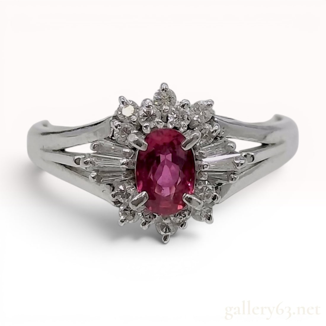 Ruby and Diamond Platinum Cluster Cocktail Ring: This vintage cocktail ring is crafted from platinum and features a central oval-faceted ruby of a pinkish-red hue. The ruby is set within a sunburst halo cluster consisting of twelve round