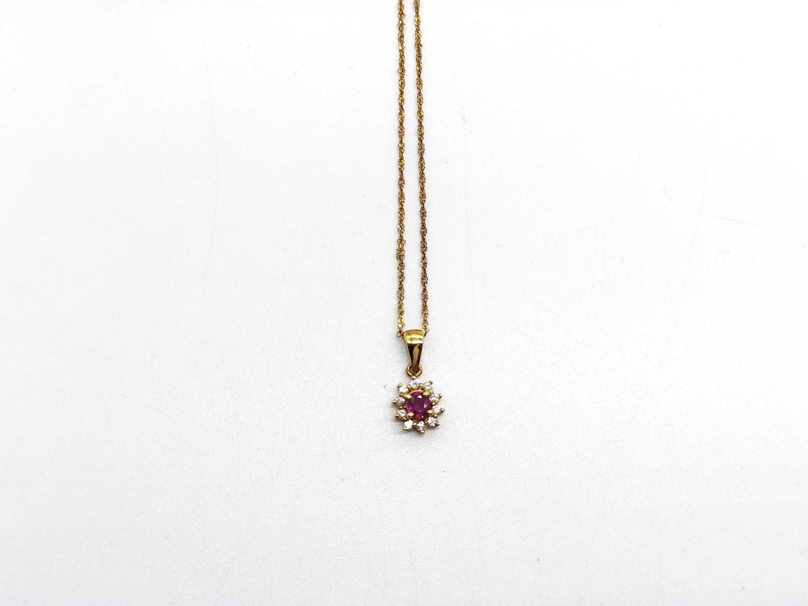 18K Yellow Gold Ruby and Diamond Halo Pendant Necklace: A gemstone cluster pendant necklace featuring a round-cut faceted red ruby center, measuring approximately 3 mm in diameter. The center stone is surrounded by a halo cluster of eight small round-cut