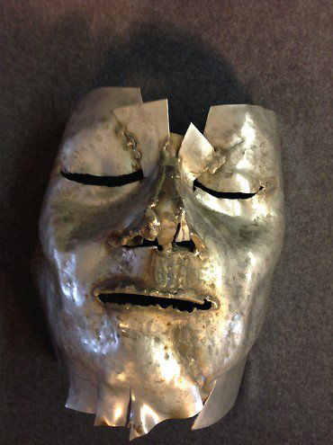 Large Metal Mask by Marian Owczarski: This metal mask has the face of a sleeping man who is dreaming. The sculpture has a variety of textures. The areas around the nose, eyes and mouth show evidence of where the metal pieces were fused to