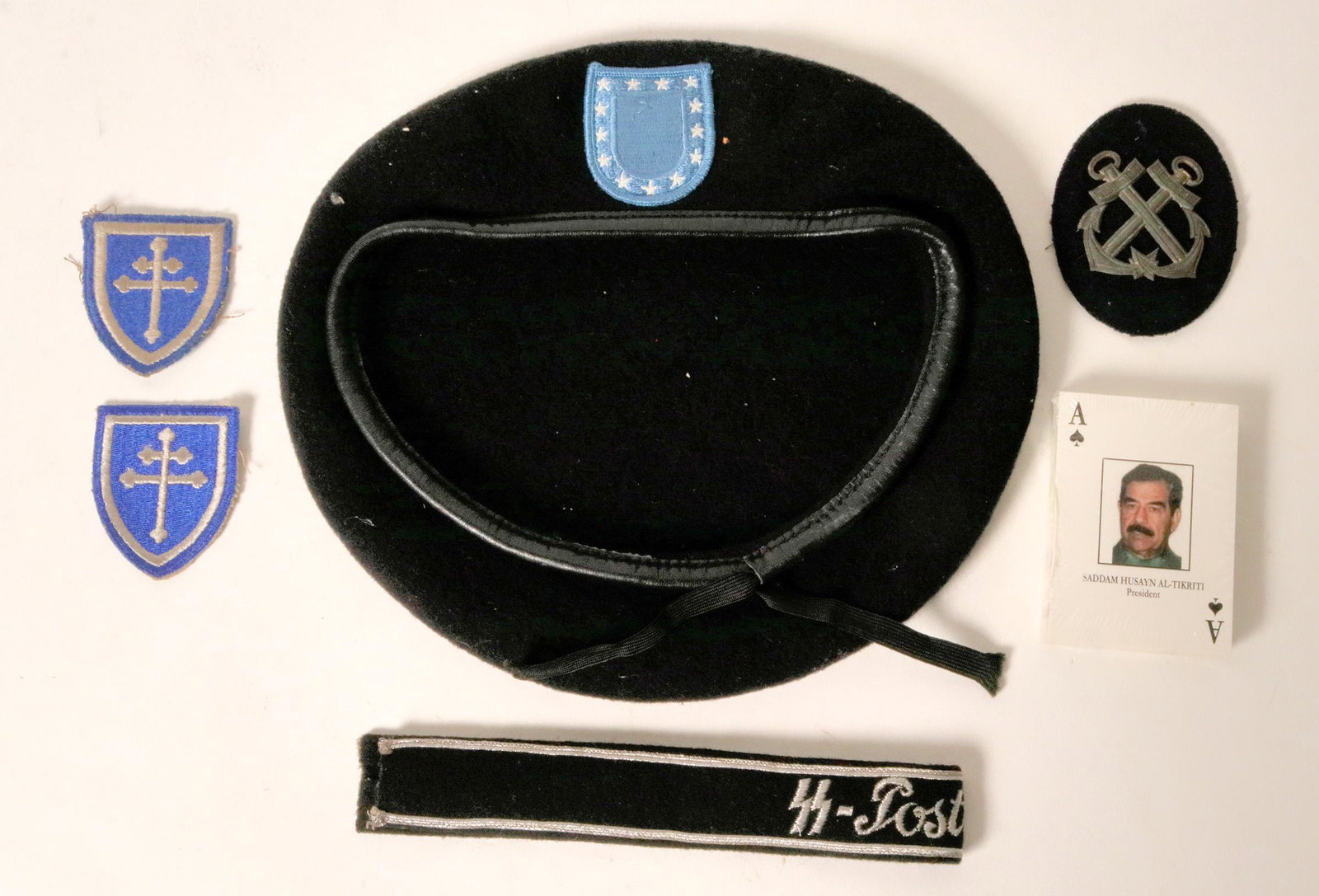 Military Collection (114948): Unopened deck of Saddam Husayn Al-Tikriti playing cards. Black beret with blue badge, three military patches, black band "SS-Postschutz" 16 inches long. Provenance: Country (if not USA): State: City/C