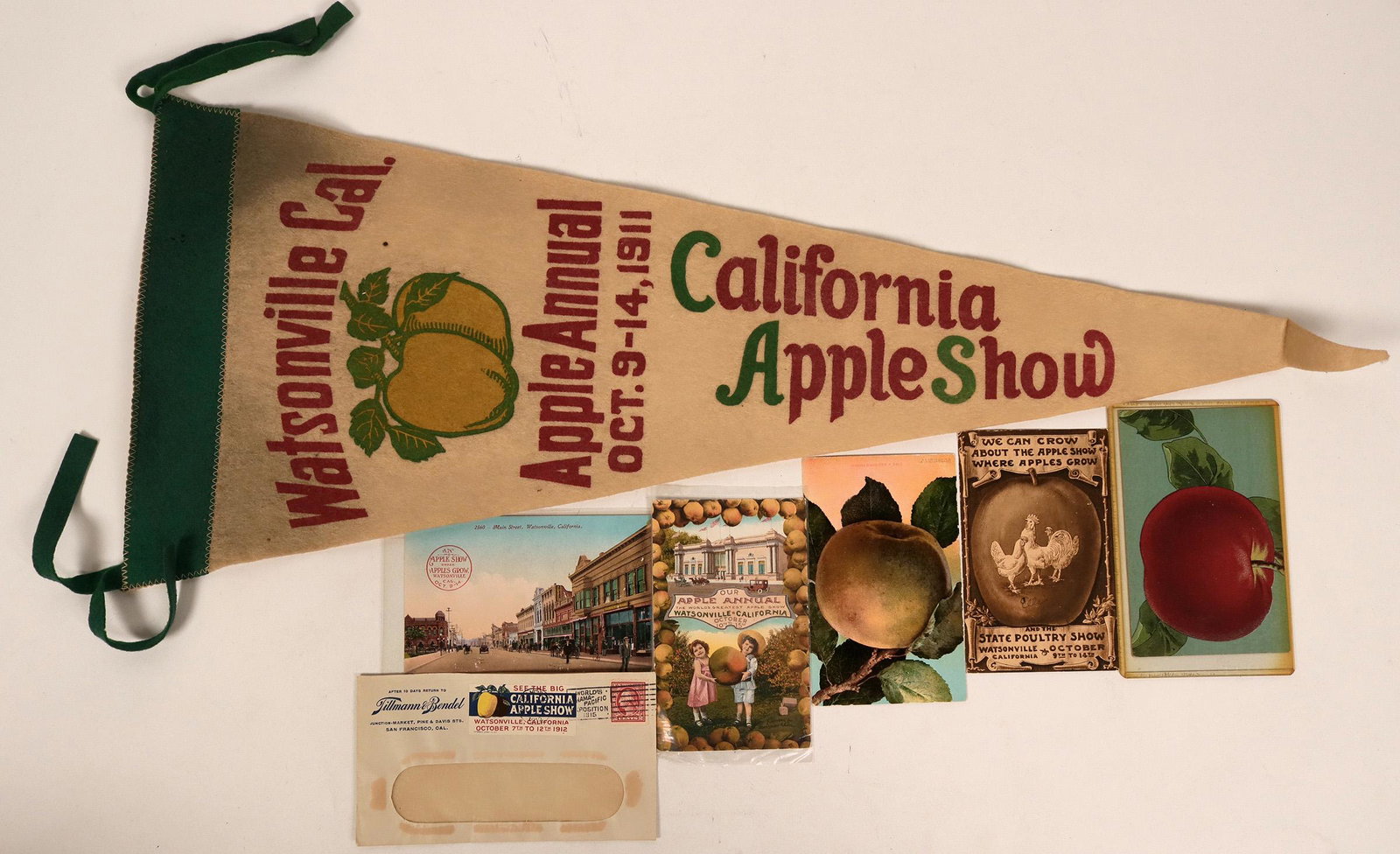 1911 Apple Show Postcards & Pennant (115557): This lot celebrates The Apple Show in Watsonville, California in 1911. It comes with a 27" pennant, a window cover and five litho postcards. All but two have writing and addresses on them. Provenance: