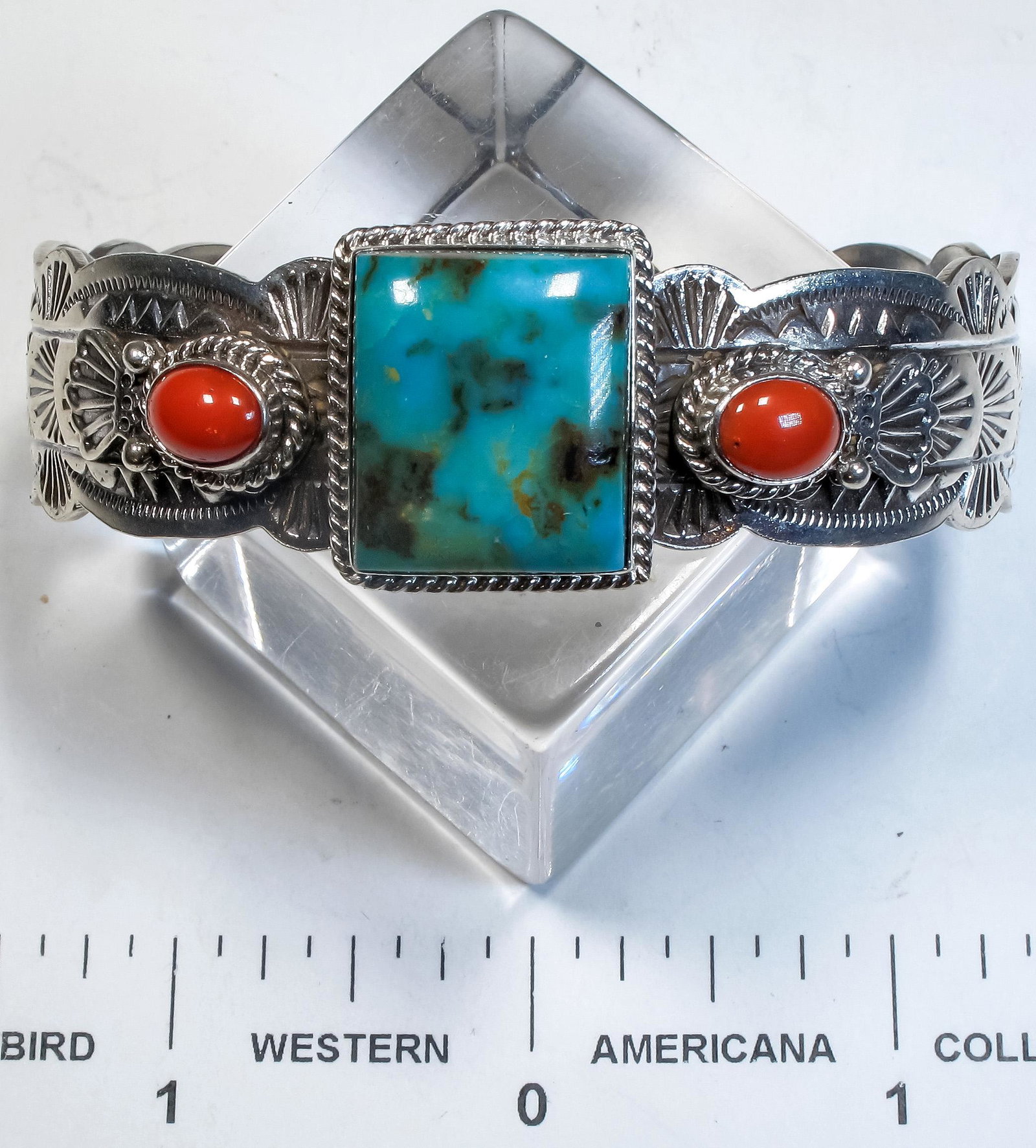 Navajo Turquoise and Coral Bracelet (125161): A beautiful Navajo sterling silver bracelet with a square cut turquoise stone set on center and flanked by two salmon colored coral stones, the engraved silver work on the band continues from the cent